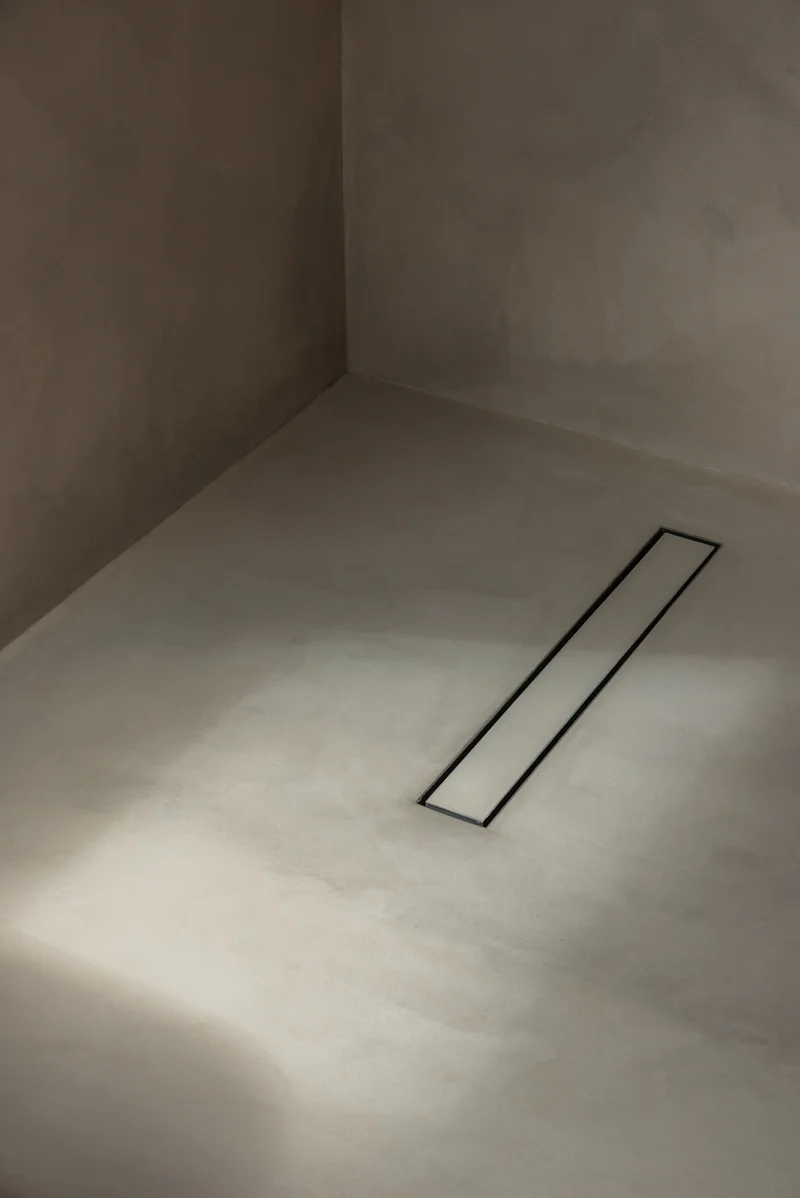Taupe seamless microcement curbless wet room floor in Park City with linear channel drain and raking sunlight