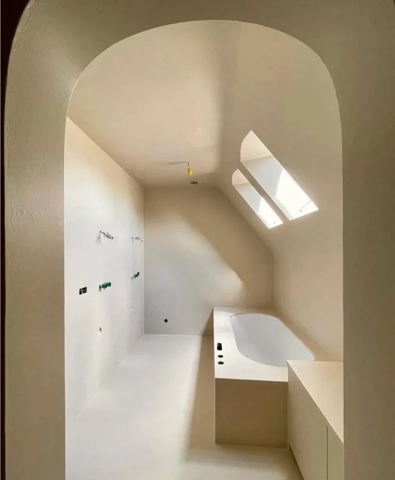 Cream vanilla microcement loft attic bathroom suite in Park City, Utah with curved barrel ceiling, arched entry, walk-in shower zone, integrated bath surround and skylights