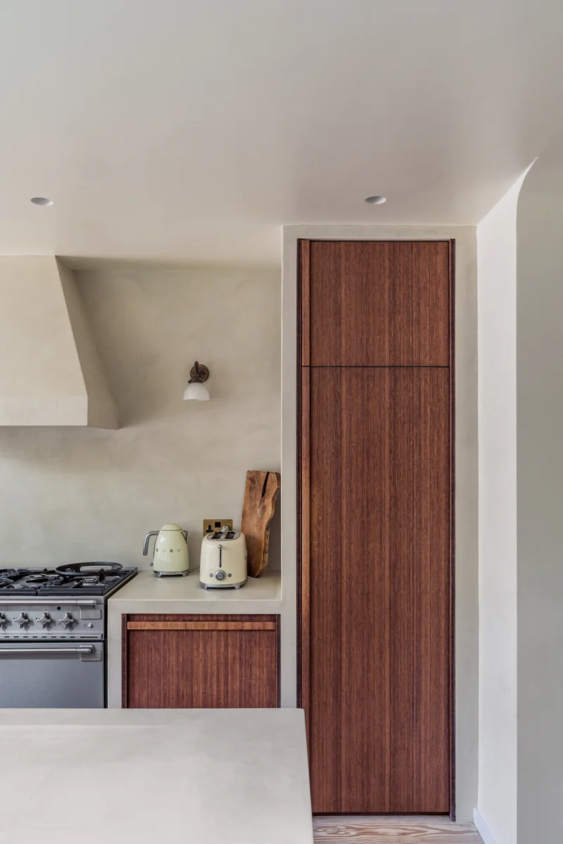 Warm ivory sculpted microcement plaster range hood canopy in Park City, Utah with integrated worktop upstand and reeded walnut cabinetry