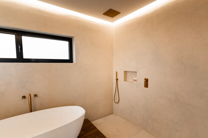 Creamy blush microcement wet room in Park City, Utah with cove LED lighting, brass rainfall shower and clerestory window