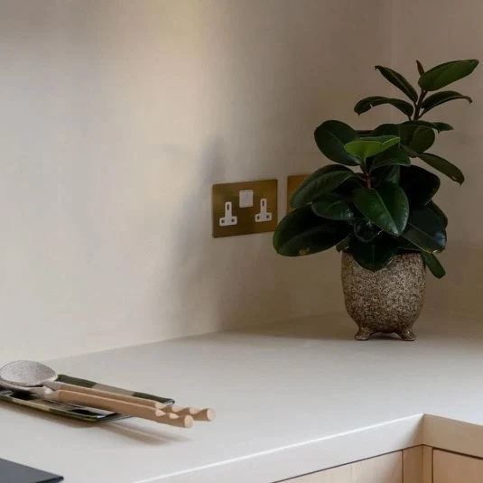 Off-white greige seamless microcement kitchen worktop and backsplash corner detail in Park City, Utah with aged brass sockets and pale oak drawers