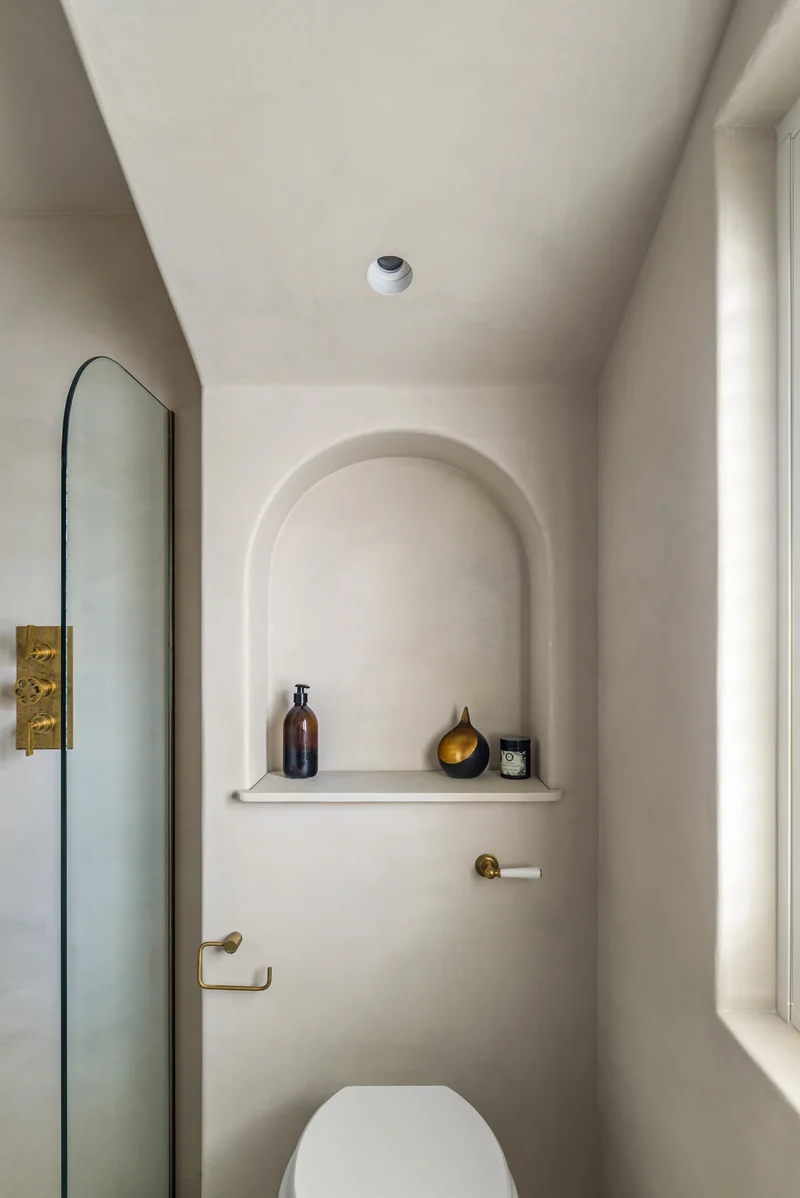 Warm ivory microcement powder room in Park City with arched plaster niche, aged brass fixtures and soft daylight