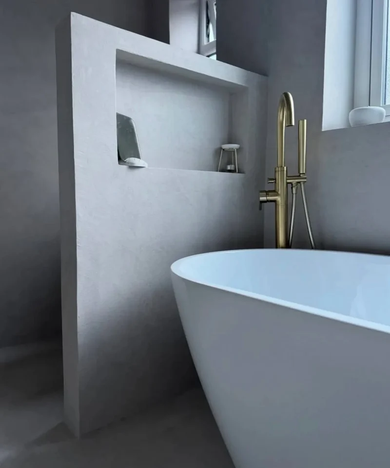 Cool-toned dove grey microcement bathroom in Park City with sculptural partition wall, recessed niche and brushed gold tub filler