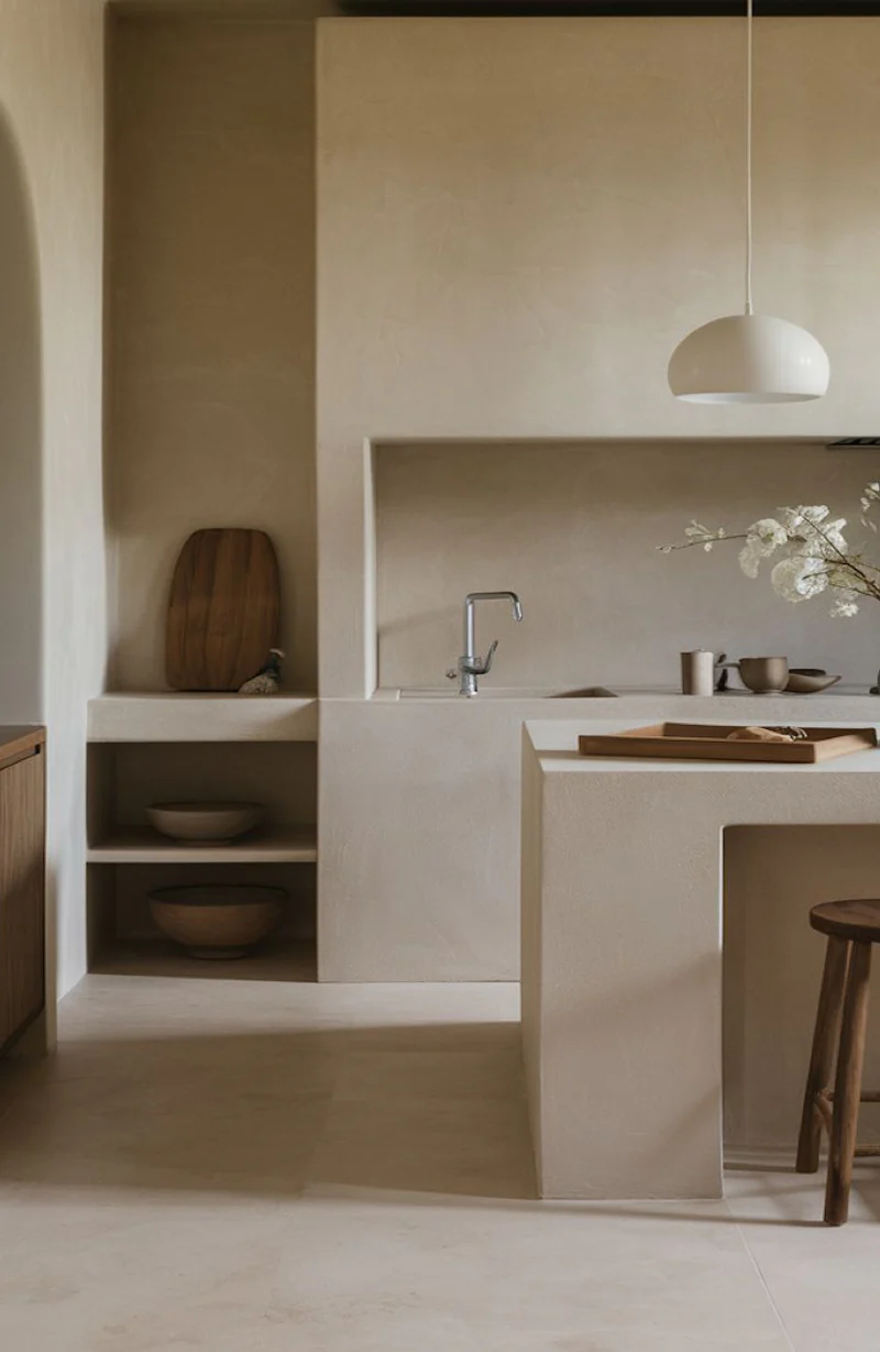 Warm sand greige monolithic cast microcement kitchen island, worktop and open shelving niche in Park City, Utah with arched doorway and dome pendant