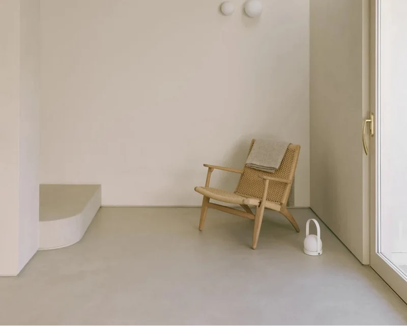 Dove grey seamless microcement living room floor in Park City, Utah with limewash plaster walls and oak paper-cord lounge chair