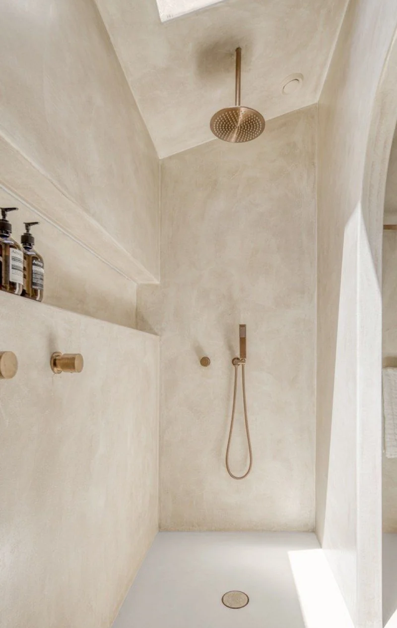 Sunlit oatmeal microcement walk-in shower in Park City loft with sloped ceiling skylight, brushed bronze rainfall and recessed ledge shelf