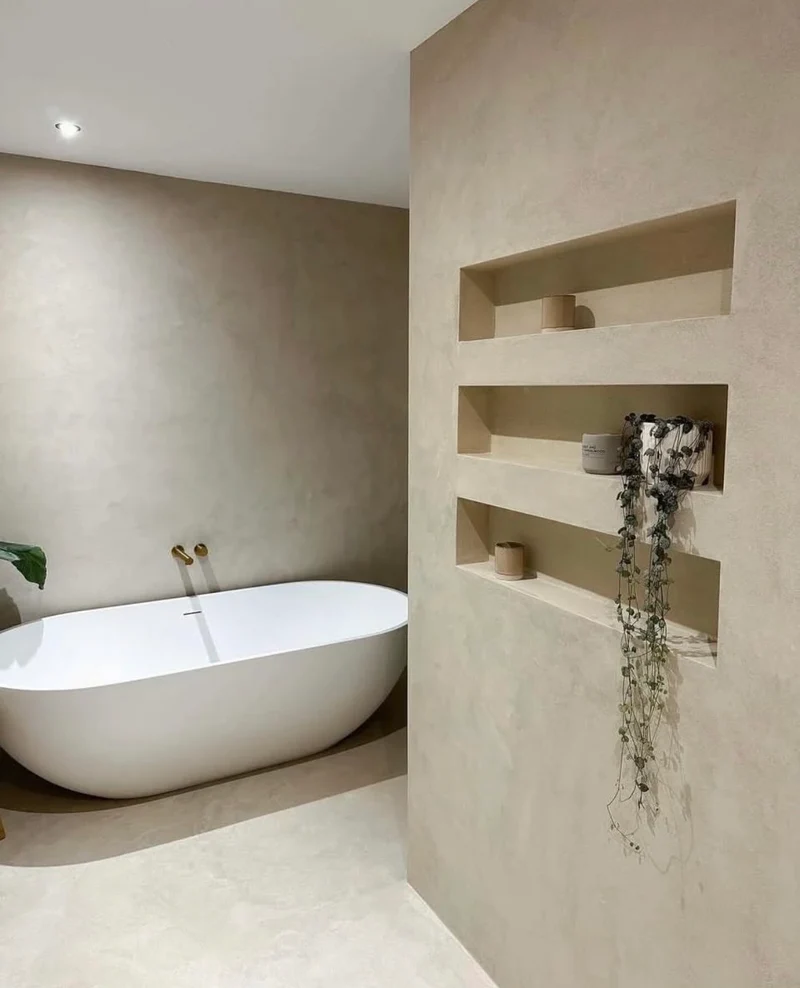 Oat sand microcement bathroom wall in Park City, Utah with freestanding tub, recessed niche shelves, brushed brass filler and trailing greenery by Jeff Mitchell