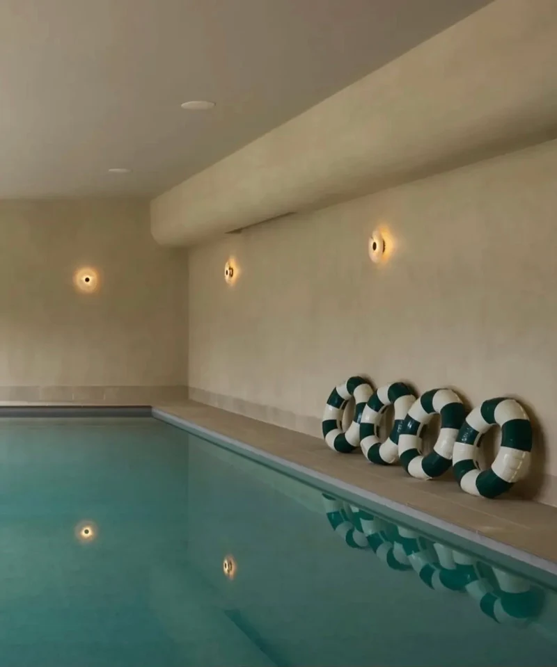 Warm cream champagne microcement indoor pool room walls in Park City, Utah with curved soffit, amber wall lights and humidity-resistant seamless finish