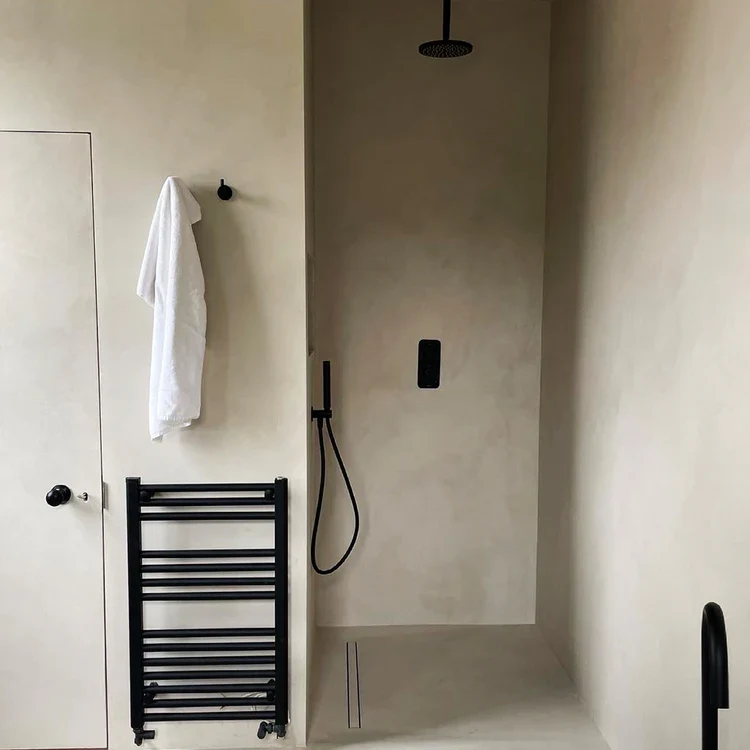Sand beige microcement walk-in shower in Park City with matte black rainfall fixtures, ladder towel radiator and curbless recessed drain
