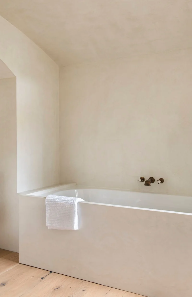 Belgian minimalist ivory limestone microcement bathroom in Park City, Utah with arched doorway and aged bronze fixtures