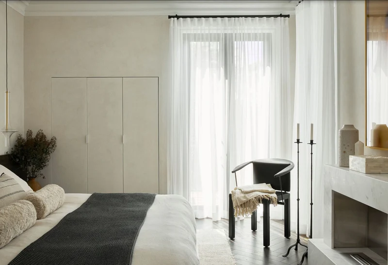 Pale greige mushroom microcement bedroom walls in Park City, Utah with flush integrated wardrobe doors, marble fireplace surround and sheer curtains