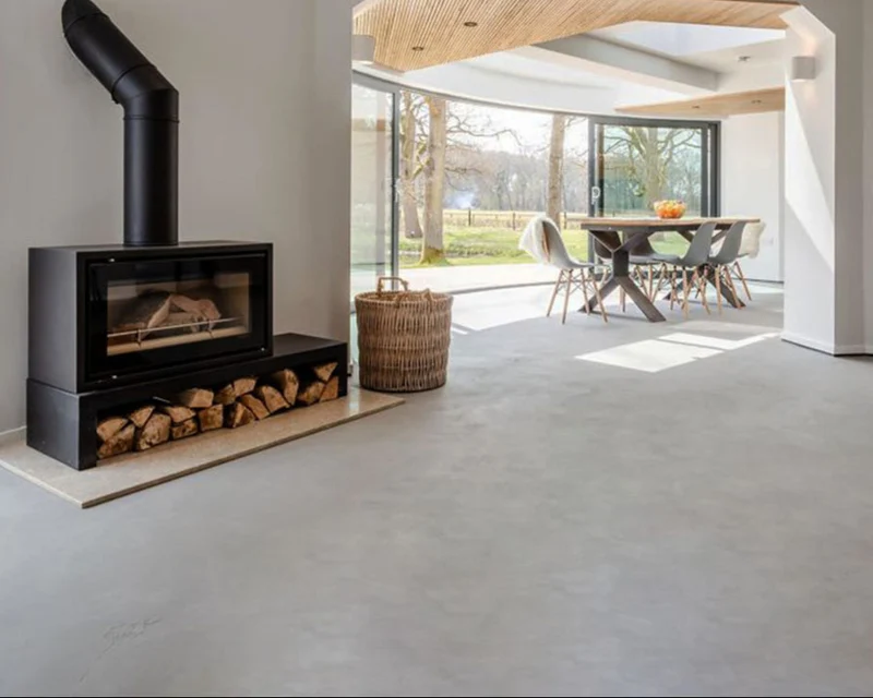 Cool pale grey microcement great room floor in Park City, Utah with seamless open-plan flow, black wood-burning stove and travertine hearth